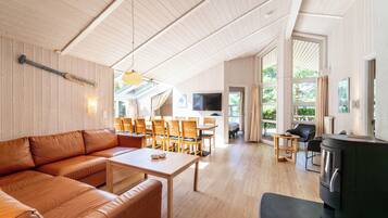 Ein gemütliches Wohnzimmer mit Ledersofa, Esstisch aus Holz und Stühlen, einem Kamin und großen Fenstern, die natürliches Licht und Ausblicke bieten.