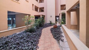 Un pasillo con piso de baldosas, rodeado de paredes con balcones y un camino bordeado de plantas.