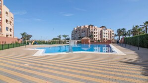 Una piscina con borde de baldosas, rodeada de edificios y palmeras.