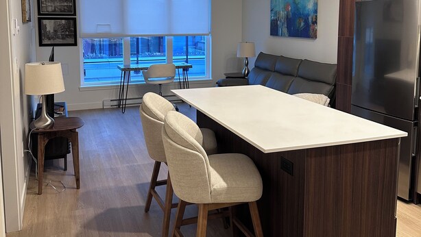 A modern kitchen with a central island, bar stools, a dining area with a view, and a large refrigerator. - Brand new condo in heart of Willoughby Town Centre Langley BC (Langley Township)