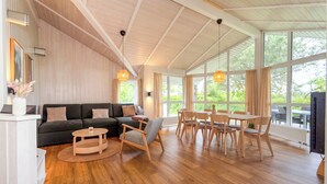 A spacious living area with a wooden ceiling, a sofa, a round coffee table, and a dining set. - Beach view vacation home 19 (Lübeck-Travemünde)