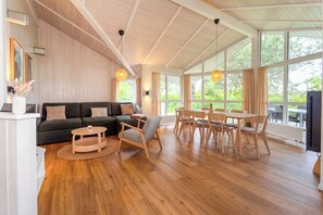 Amplia sala de estar con techo de madera, un sofá, una mesa de centro redonda y un juego de comedor.