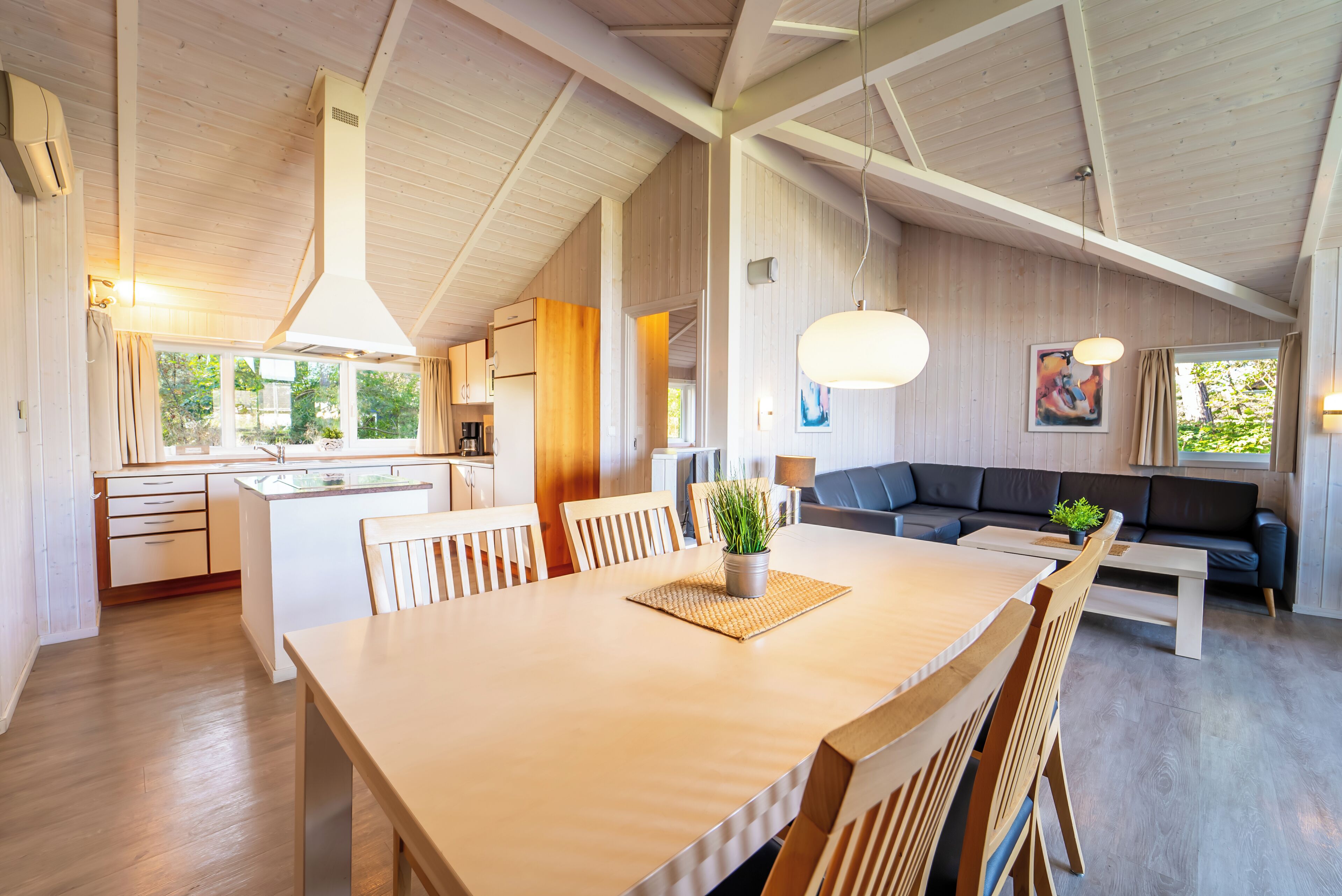 Amplia sala de estar con una gran mesa de comedor de madera, un sofá y una cocina al fondo.