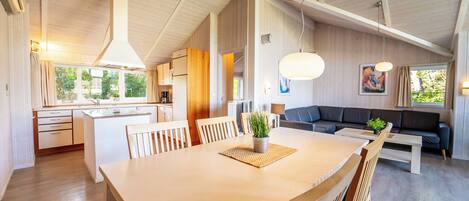 Amplia sala de estar con una gran mesa de comedor de madera, un sofá y una cocina al fondo.