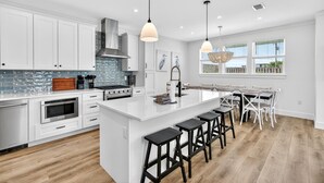 A modern kitchen with white cabinetry, a central island, bar stools, and pendant lighting. - Oceans East: Private heated pool, Free golf cart, 1 min beach, Game & Bunk rooms (Miramar Beach)