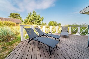A wooden deck with two lounge chairs and a small table, surrounded by a white fence and tall grass. - Beach view vacation home 25 (Lübeck-Travemünde)