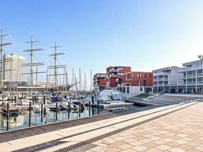 A marina with several tall ships docked, modern buildings, and a clear sky. - Beach view vacation home 14 (Lübeck-Travemünde)