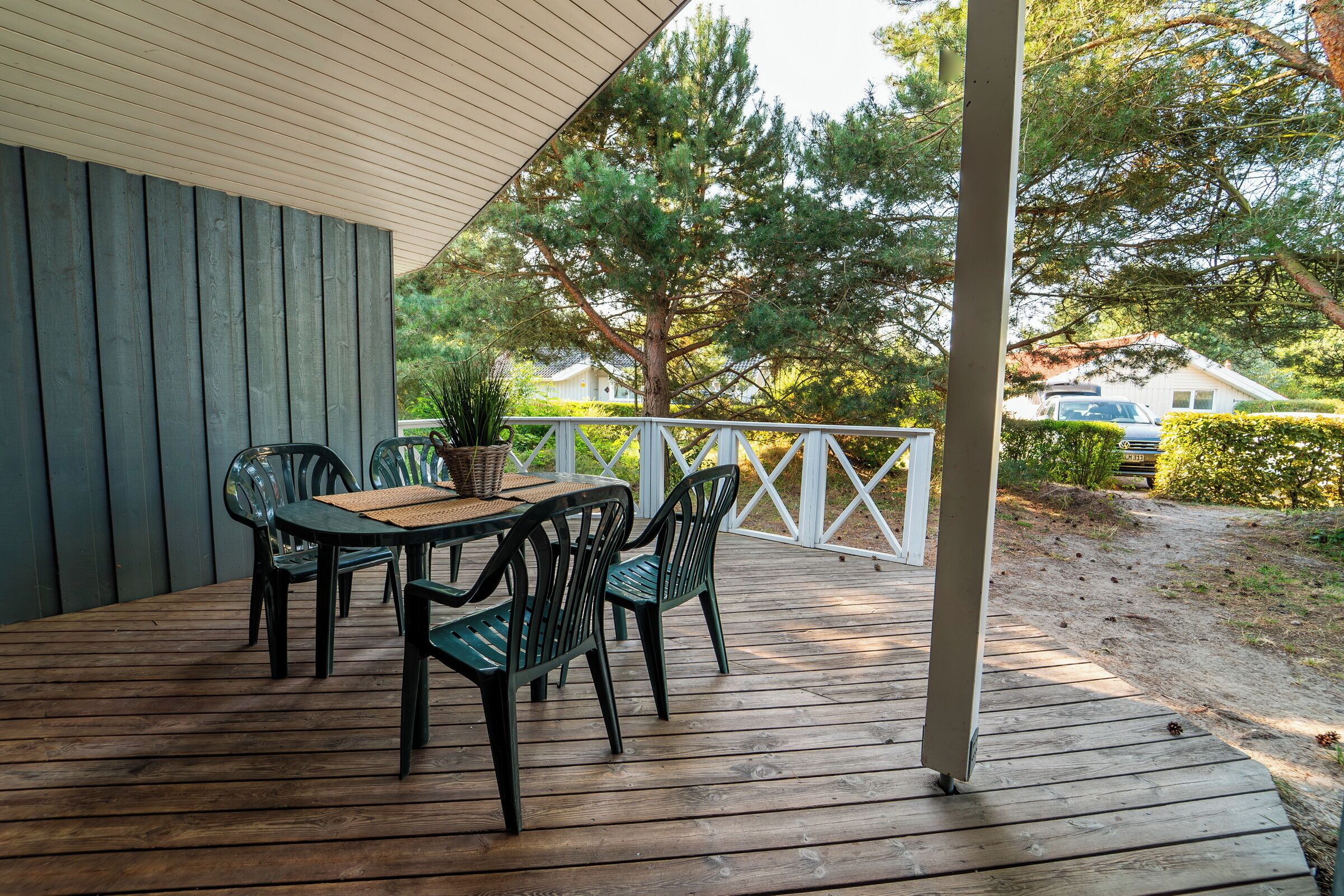 A wooden deck with a table and chairs, surrounded by a white railing and trees.