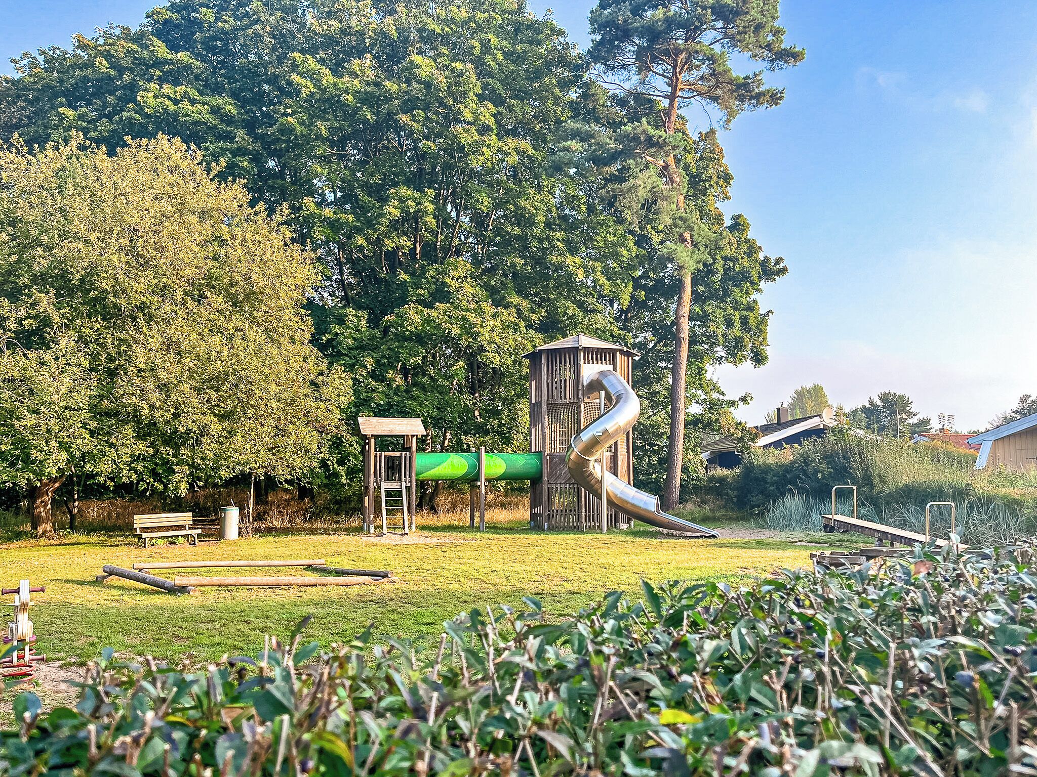 Un parque infantil con tobogán y estructuras para escalar, rodeado de árboles y césped.