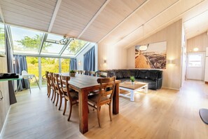 Ein geräumiger Wohnbereich mit einem Holzespeisebereich und Stühlen, einem schwarzen Ledersofa und einem großen Fenster mit Blick ins Freie.