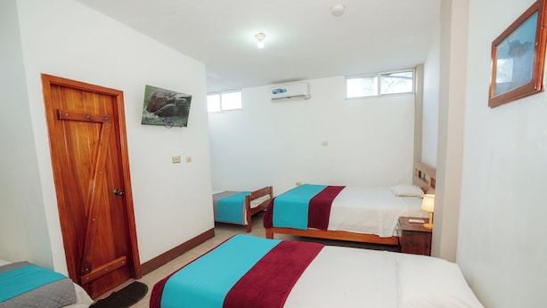 A hotel room with three beds, a wooden door, an air conditioning unit, and a small window. - El Descanso del Petrel (Puerto Ayora)