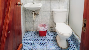 A bathroom with a wooden door, a sink, a toilet, a mirror, and a tiled floor. - El Descanso del Petrel (Puerto Ayora)