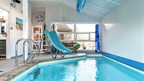 Una piscina interior con tobogán, escalera y vistas al exterior.
