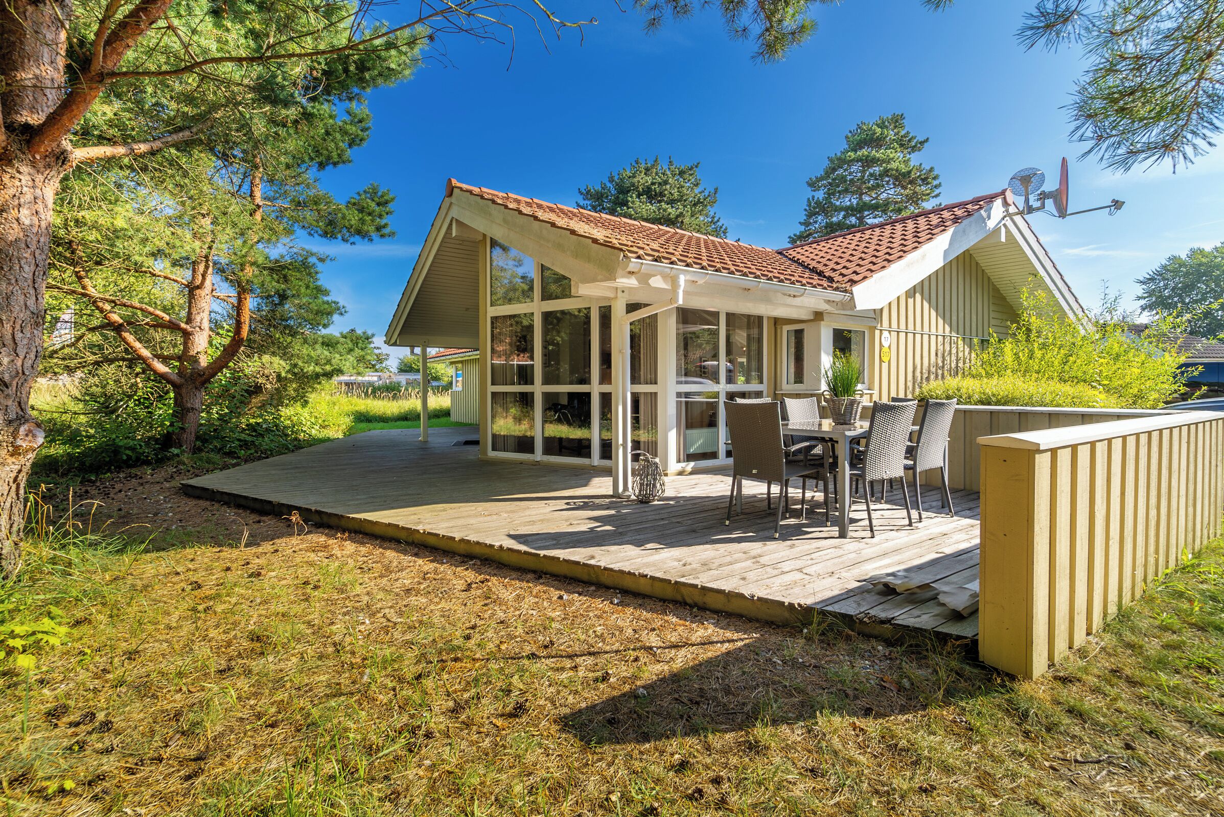 Ein Haus mit überdachter Terrasse, einem Essbereich mit Stühlen und einem großen Fenster mit Blick auf eine Rasenfläche.