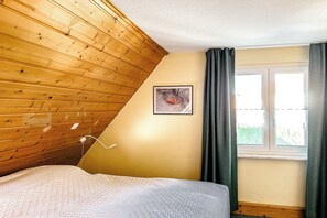 Une chambre avec un plafond en pente, un lit, une fenêtre avec des rideaux et un tableau encadré au mur.