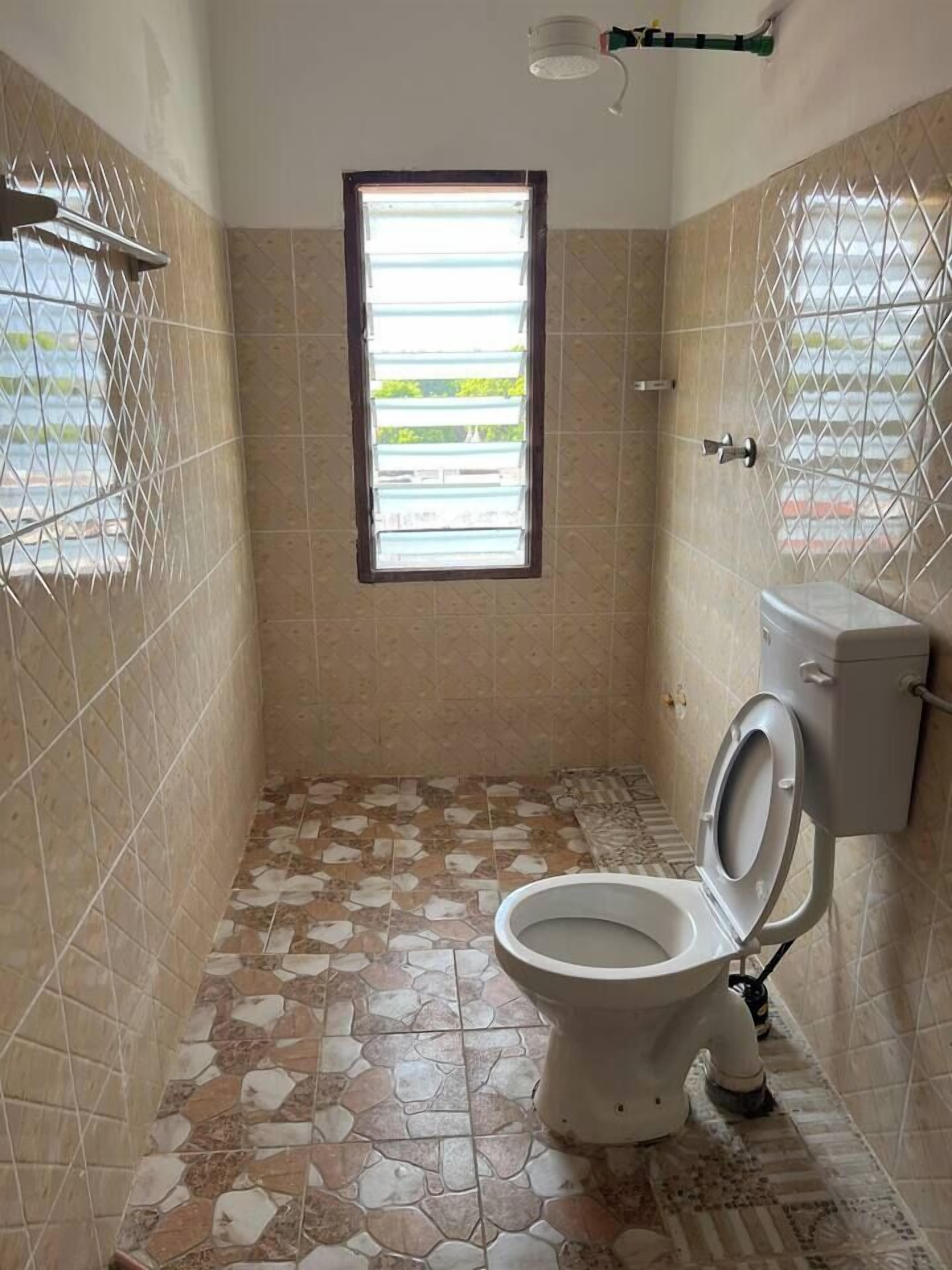 A bathroom with a toilet, a window, and tiled walls.