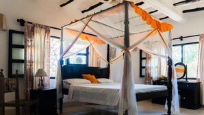 A bedroom with a four-poster bed, a nightstand, a chair, and a window with curtains.