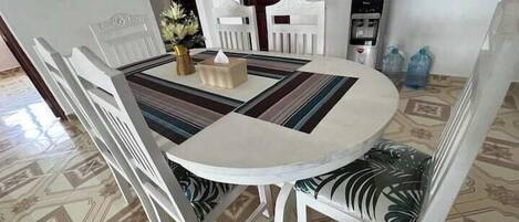 A dining area with a round table, white chairs, and a water dispenser.