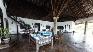 A spacious room with a large bed, wooden furniture, a staircase, and a thatched roof.