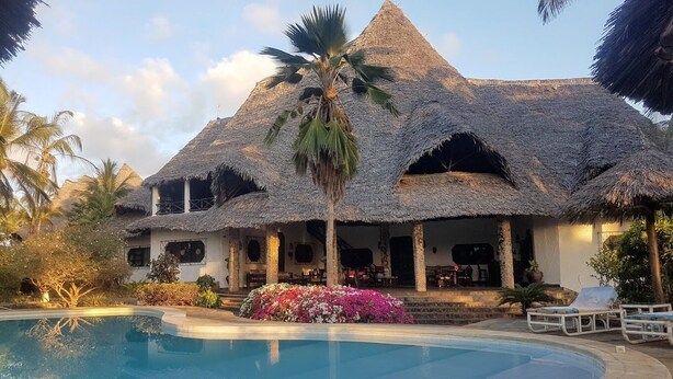 A resort with a pool, thatched-roof buildings, and palm trees.