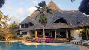 Ein Resort mit Pool, strohgedeckten Gebäuden und Palmen.