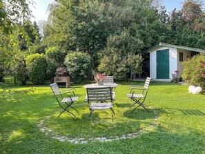 A garden with a wooden table and chairs, surrounded by lush greenery and a small shed. - Guesthouse Karstadt Apartment 04 - Limone - Ostseebad Boltenhagen (Ostseebad Boltenhagen)