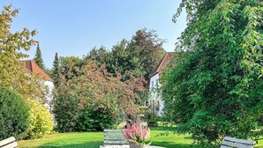 A garden with a round table and four wooden chairs, surrounded by lush greenery and trees. - Guesthouse Karstadt Apartment 04 - Limone - Ostseebad Boltenhagen (Ostseebad Boltenhagen)