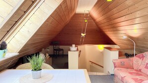 An attic bedroom with wooden slats on the ceiling, a small table with a plant, a pink sofa, and a chair. - Guesthouse Karstadt Apartment 04 - Limone - Ostseebad Boltenhagen (Ostseebad Boltenhagen)