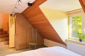 A bedroom with a sloped ceiling, a bed, a chair, a ladder, and a window with a plant. - Guesthouse Karstadt Apartment 04 - Limone - Ostseebad Boltenhagen (Ostseebad Boltenhagen)