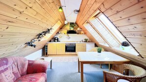 A cozy attic bedroom with wooden walls, a bed, a window, and a small kitchenette. - Guesthouse Karstadt Apartment 04 - Limone - Ostseebad Boltenhagen (Ostseebad Boltenhagen)