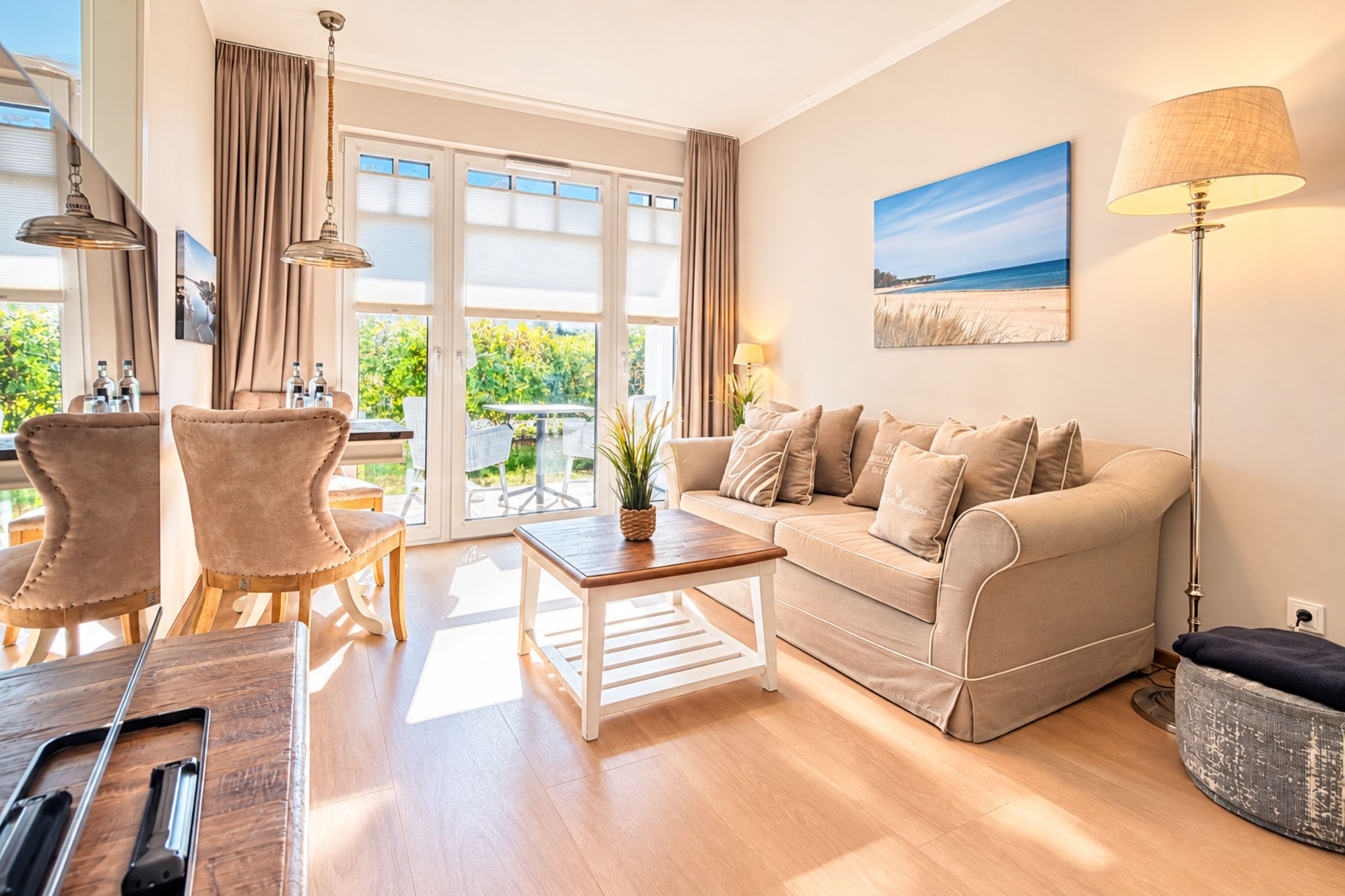Een woonkamer met een bank, twee fauteuils, een salontafel en een lamp. Er is een raam met gordijnen, een schilderij aan de muur en uitzicht op groen.