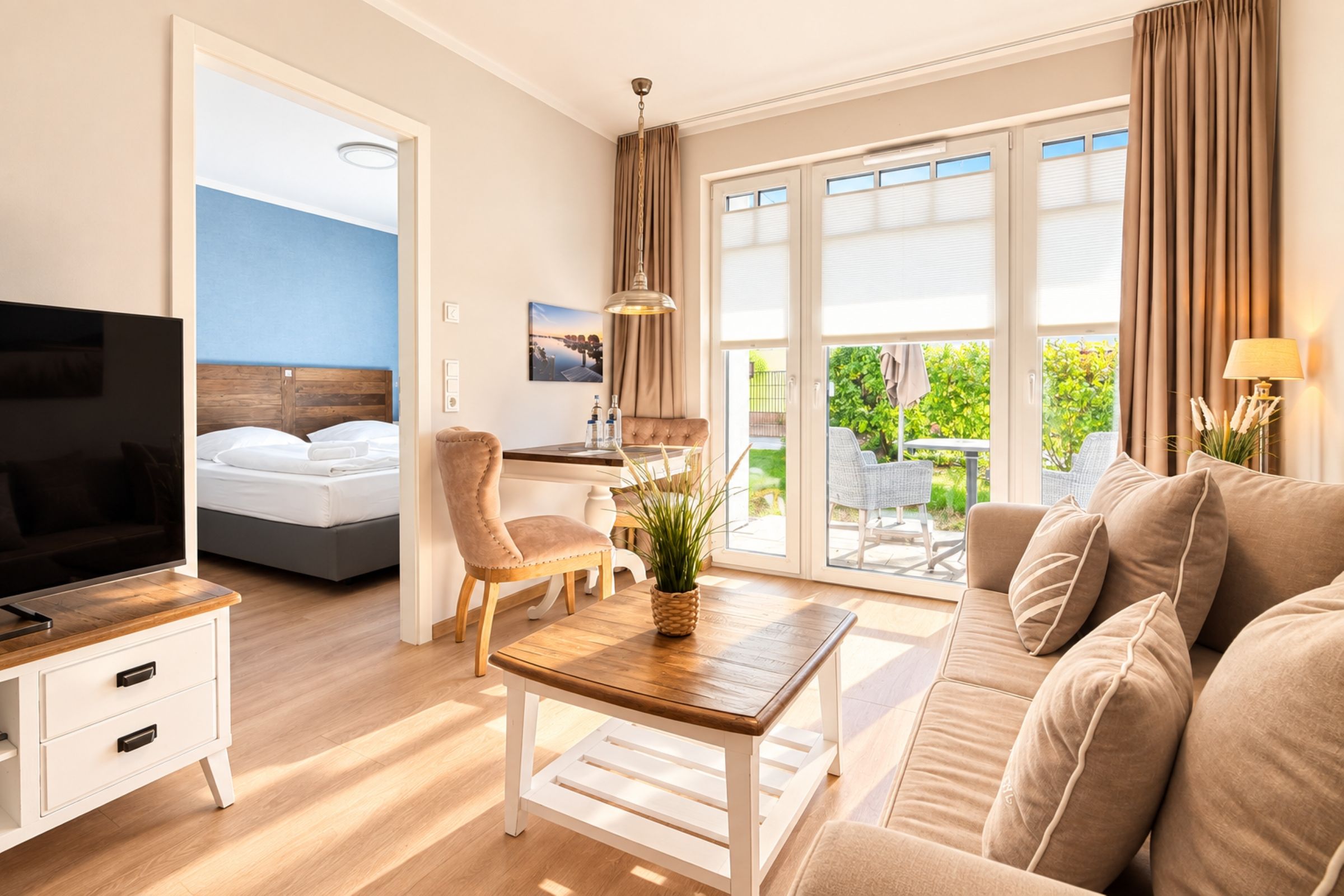 A modern hotel room with a bed, TV, seating area, and a view of greenery.