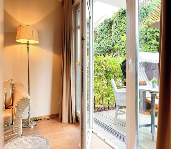 Habitación con sofá, lámpara y puerta corrediza de vidrio que da a un área exterior con mesa y sillas.