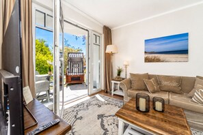 Una sala moderna con un sofá, una mesa de centro y un televisor. Hay una puerta corrediza de vidrio que da a un espacio exterior con una mesa y sillas.