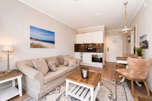 A modern living room with a beige sofa, a coffee table, and a dining area with a chair. - Baltischer Hof Apartment 03 (Ostseebad Boltenhagen)
