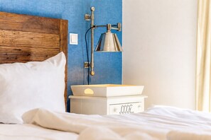 A neatly made bed with white linens, a wooden headboard, a bedside table with a lamp, and a small white drawer. - Baltischer Hof Apartment 03 (Ostseebad Boltenhagen)