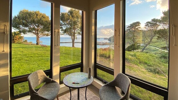 A room with large windows, two chairs, and a small table. - Most Spectacular Ocean Views - Studio (Port Orford)