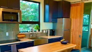 A modern kitchen with a wooden island, dark blue cabinets, stainless steel appliances, and a view of greenery outside. - Most Spectacular Ocean Views - Studio (Port Orford)