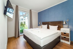 Ein Schlafzimmer mit einem Bett, einem an der Wand montierten Fernseher, einem Nachttisch und einem Fenster mit Vorhängen.
