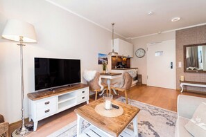A modern living room with a flat-screen TV, a dining area with a wooden table and chairs, and a kitchen with a coffee machine. - Baltischer Hof Apartment 15 (Ostseebad Boltenhagen)