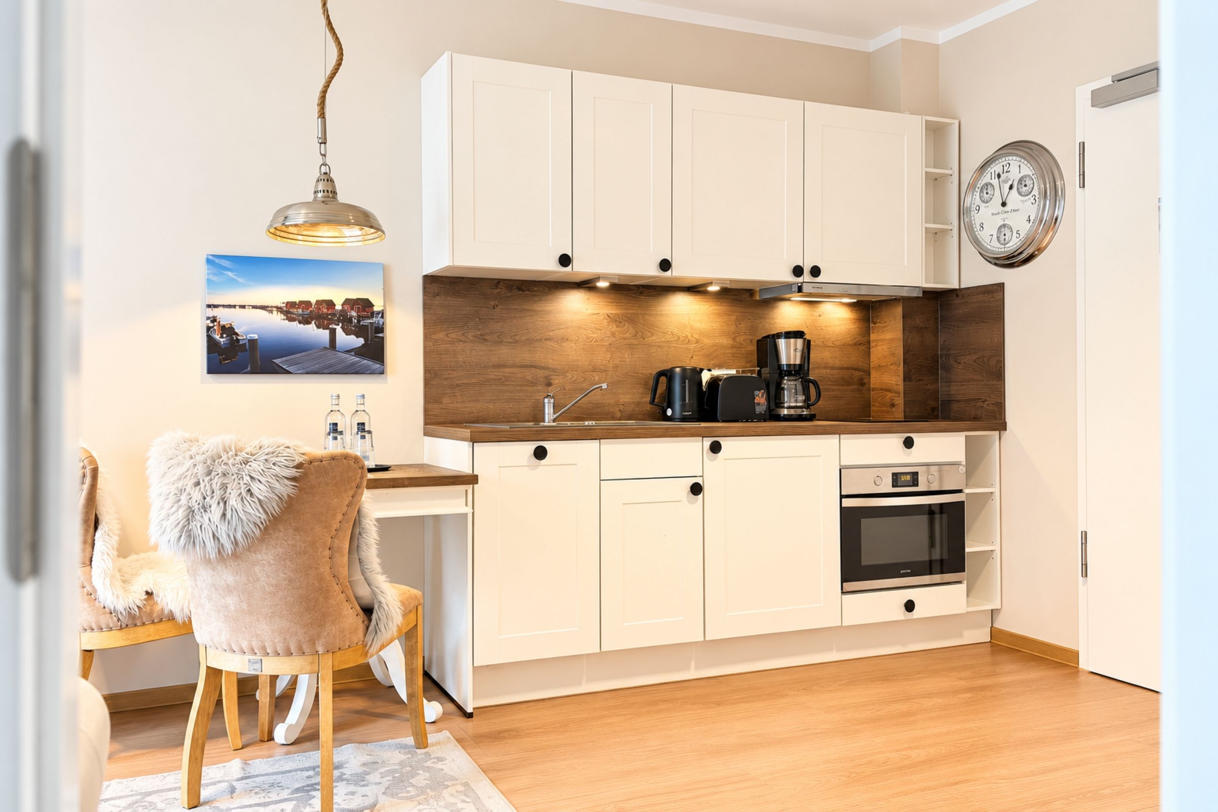 Een compacte keuken met witte kasten, een houten aanrecht, een koffiezetapparaat en een klok aan de muur.