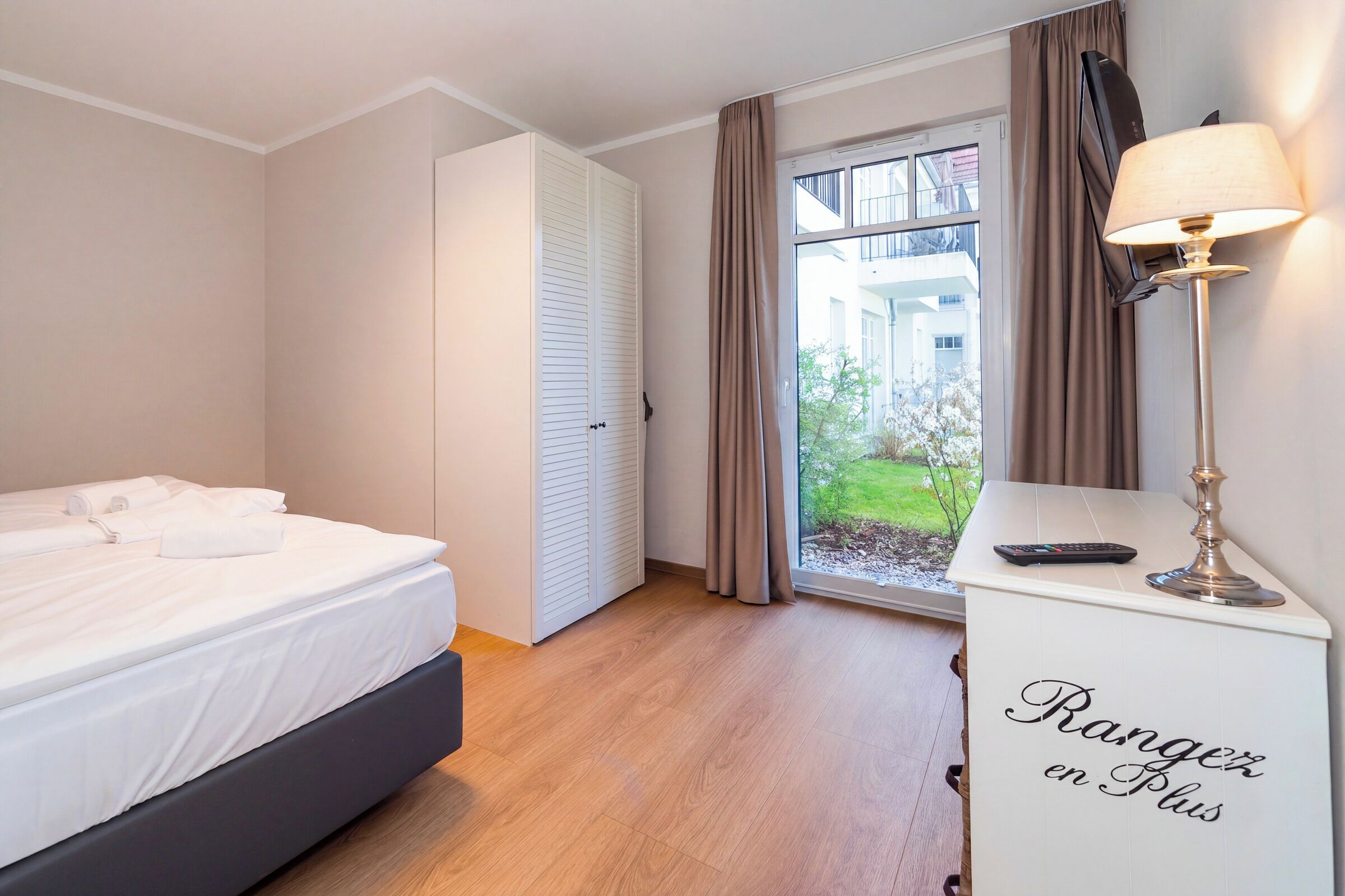 Een hotelkamer met een bed, een bureau met lamp, een kledingkast en uitzicht op buiten.