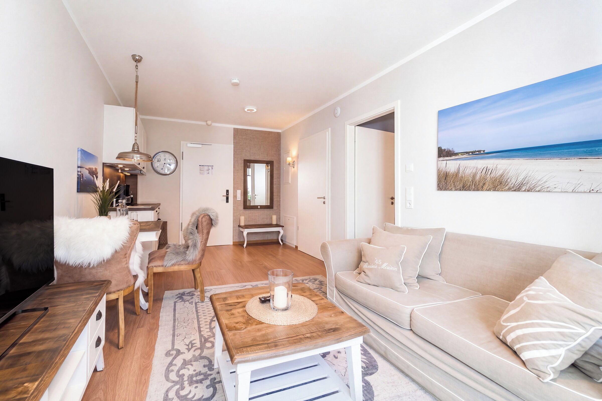 Ein modernes Wohnzimmer mit Sofa, Couchtisch und Fernseher. Es gibt einen Essbereich mit Tisch und Stühlen. Das Zimmer verfügt über ein großes Fenster mit Blick auf den Strand.