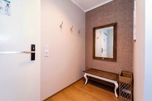 Un couloir avec un banc en bois, un miroir fixé au mur et une porte dotée d’une poignée.