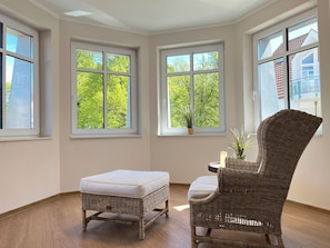 A room with a wicker chair, an ottoman, and a small table with a candle and a plant. - Baltischer Hof 21 Apartment (Ostseebad Boltenhagen)