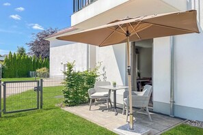 Eine Terrasse im Freien mit Tisch und Stühlen, einem beigen Sonnenschirm und Blick auf das Haus.