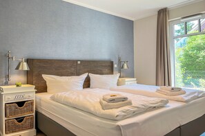 Ein Hotelzimmer mit einem großen Bett, zwei Nachttischen, einem Beistelltisch und einem Fenster mit Vorhängen.