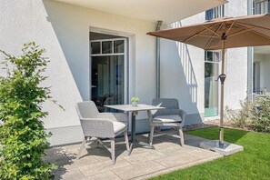 A patio with two wicker chairs and a table, a potted plant, and a large umbrella. - Baltischer Hof Apartment 04 (Ostseebad Boltenhagen)