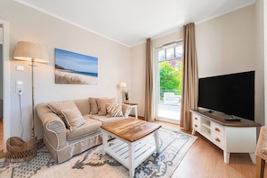 Ein modernes Wohnzimmer mit Sofa, Couchtisch, Fernseher und einem Gemälde einer Strandansicht.