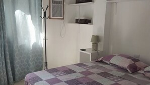 Un dormitorio con cama, mesita de noche con lámpara, estante con cestas y ventana con cortinas.
